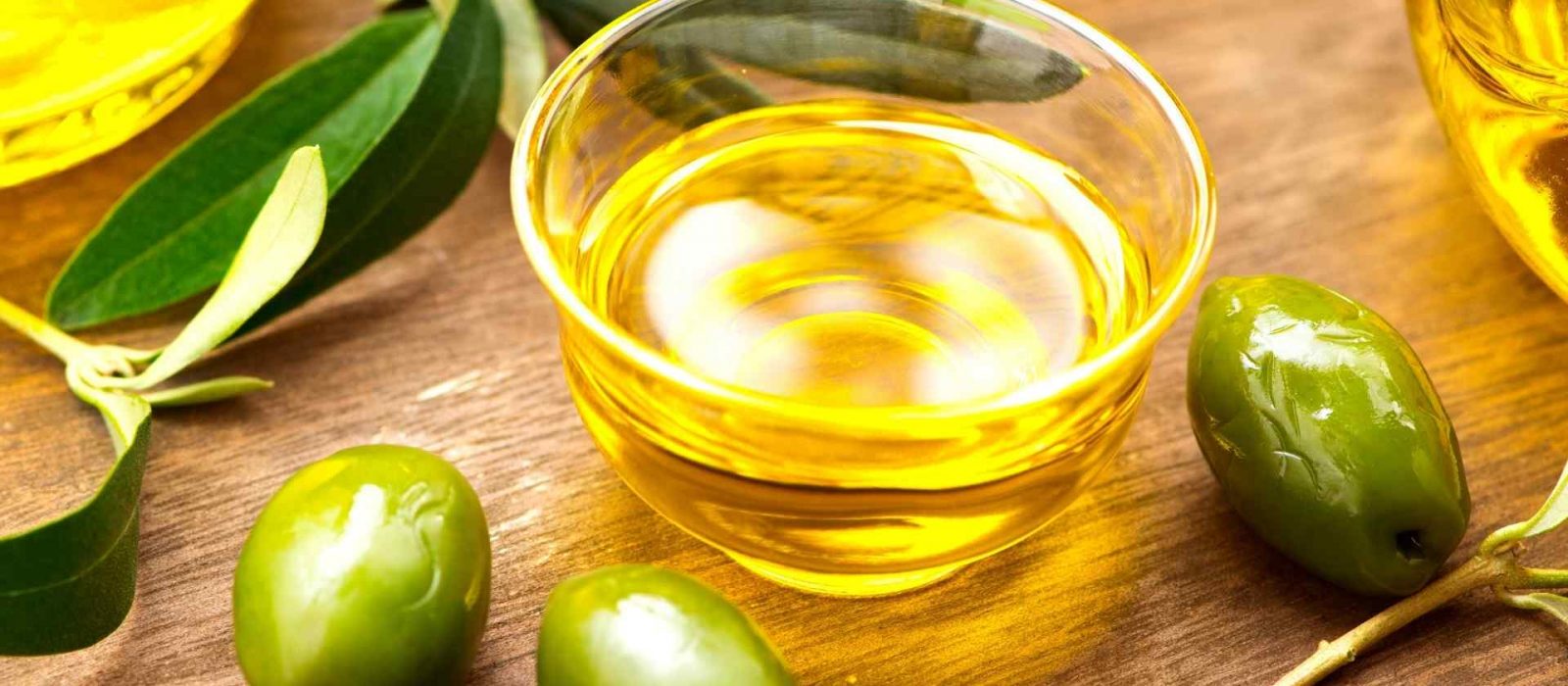 Piccola coppa di olio evo su tavolo e circondato da olive verdi